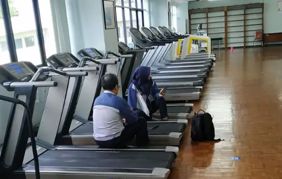 Teknisi service treadmill sedang memperbaiki bagian motor dan belt